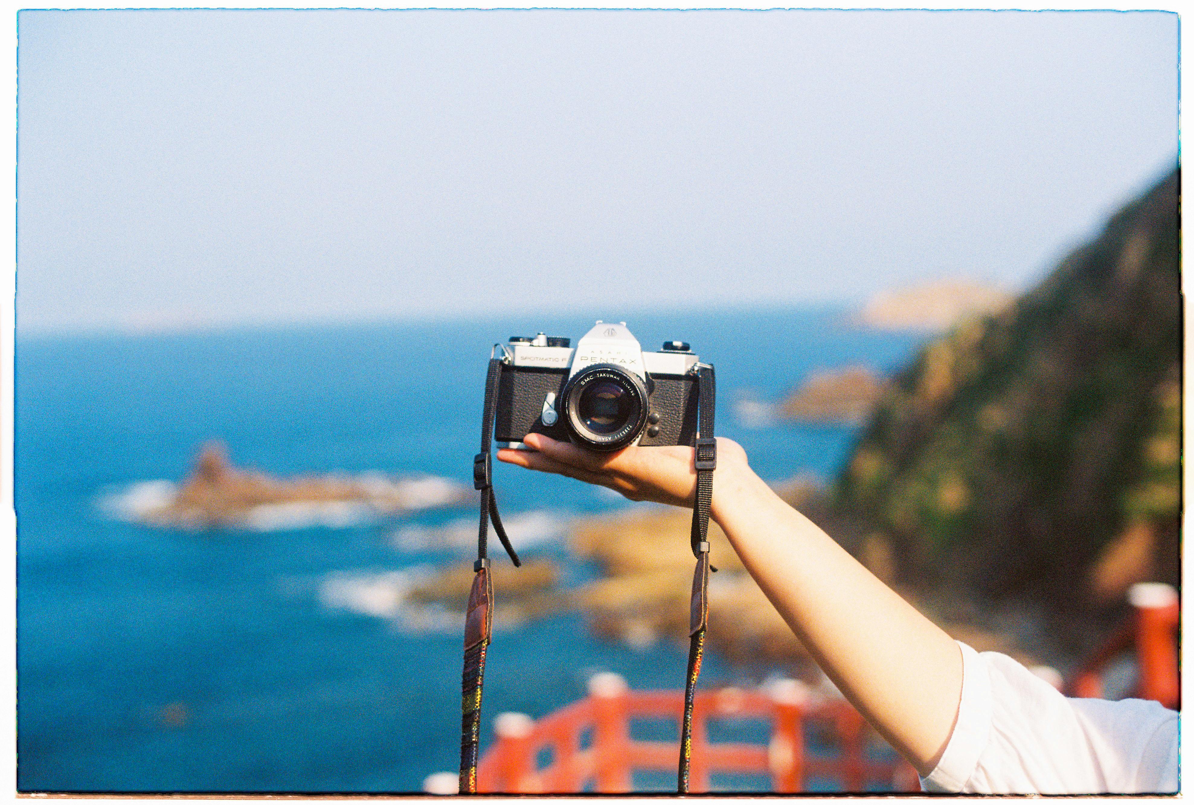 A hand holds a vintage camera against the scenic Bình Định coastline, Vietnam.