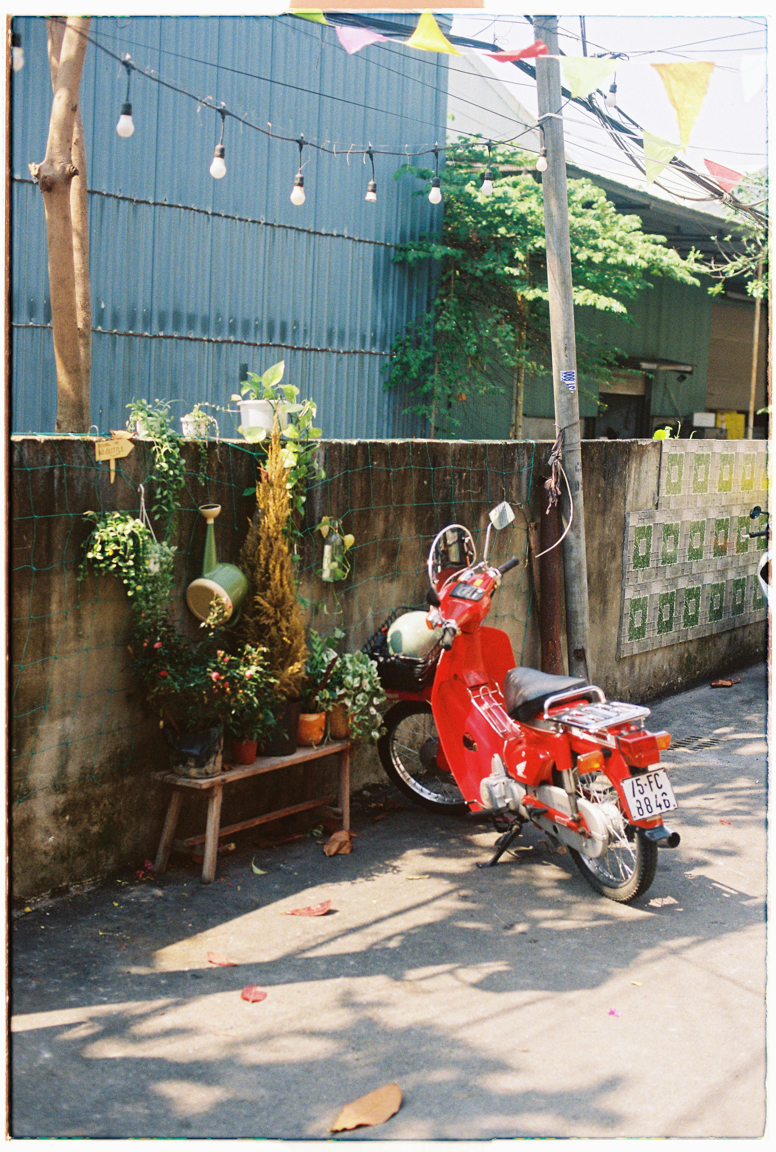 A vibrant red moped parked against a stone wall on a sunny street in Da Nang, Vietnam.