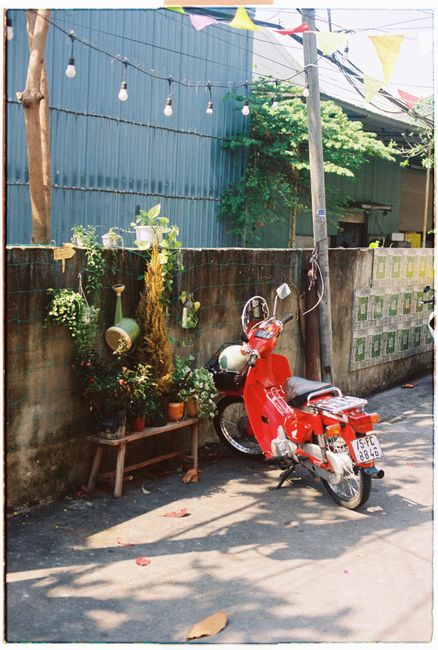 A vibrant red moped parked against a stone wall on a sunny street in Da Nang, Vietnam.
