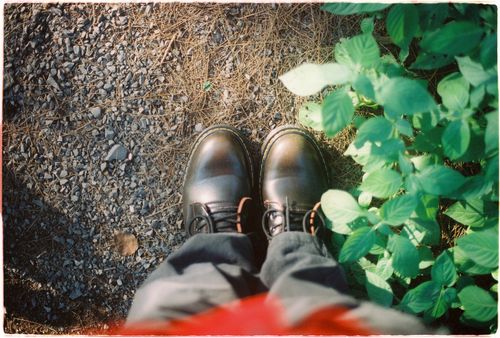 Free Artistic perspective of sturdy boots on gravel next to vibrant greenery in natural light. Stock Photo
