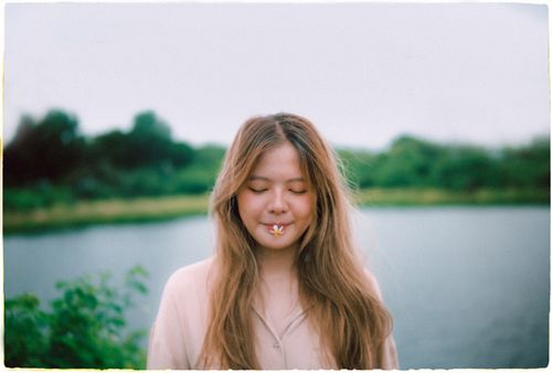 Free A serene moment as a young woman stands by a lake, eyes closed with a flower resting on her lips in Ho Chi Minh City. Stock Photo