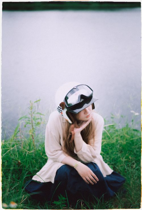 Free Woman in a helmet and goggles sitting by a riverside in Vietnam, exuding a serene, reflective mood. Stock Photo