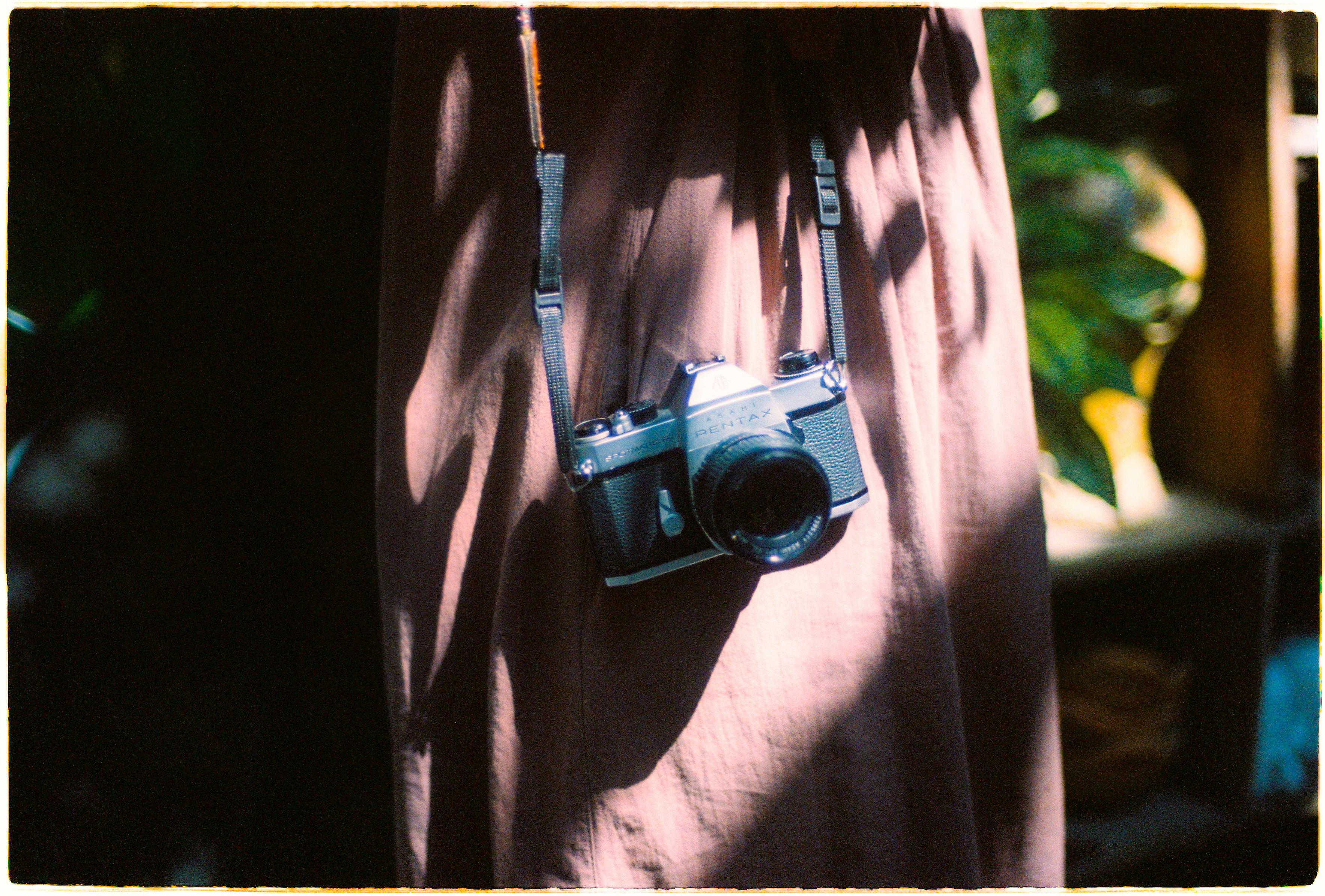 A film camera hangs against a brown dress, bathed in natural light and shadows.