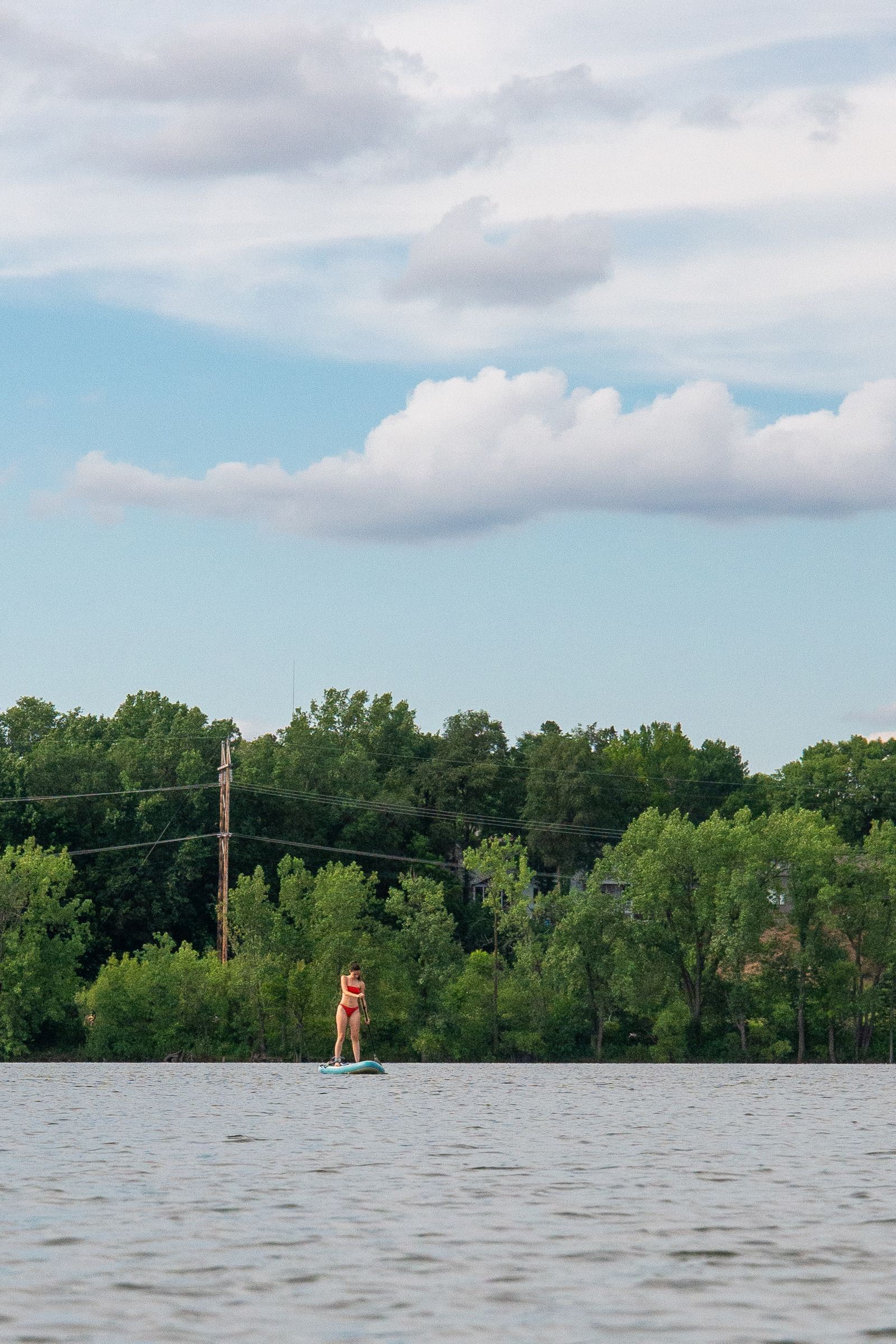 Paddler using a stand-up paddleboard on a calm lake during a recreational water outing