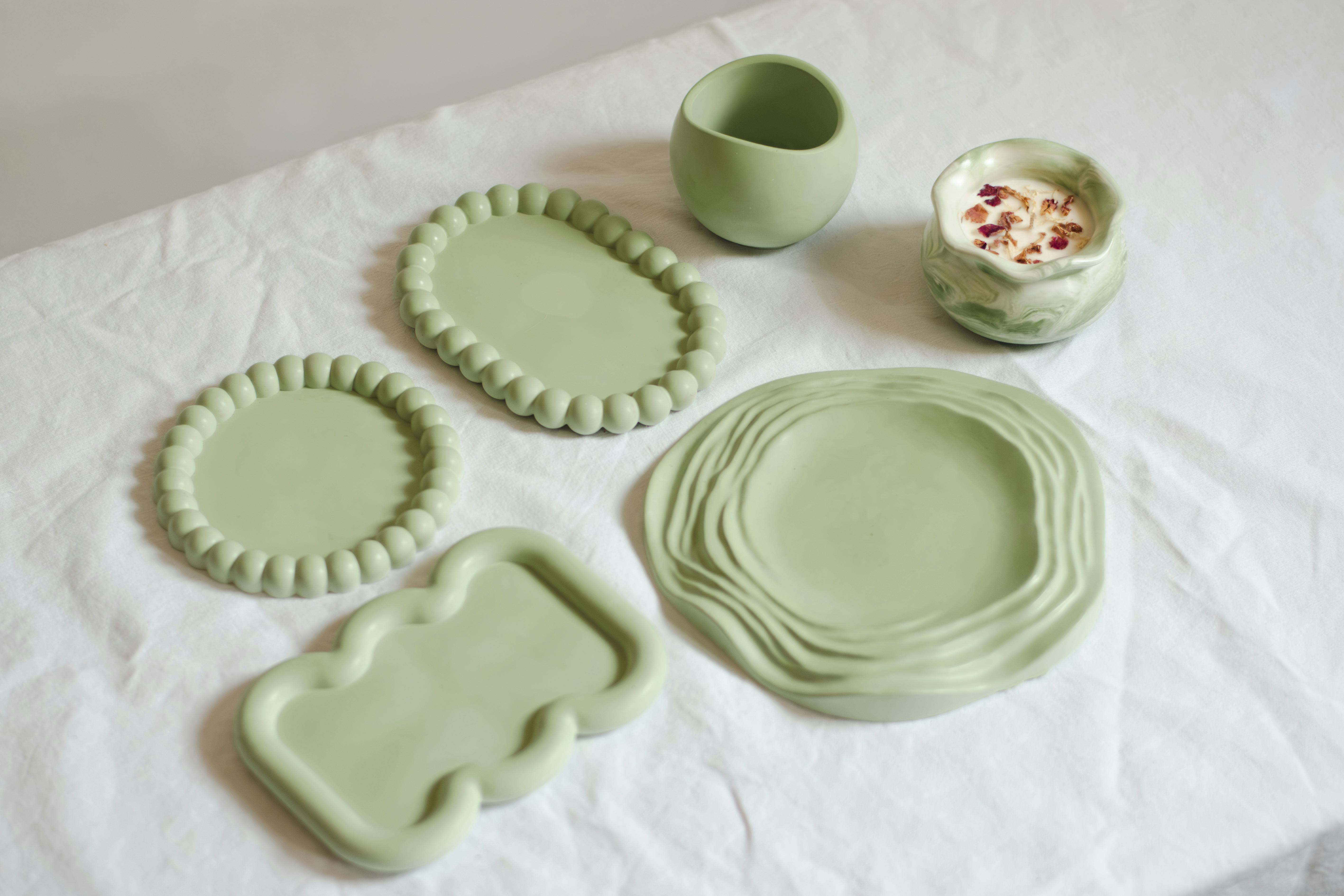 A selection of minimalist green ceramic dishes on a white table, ideal for modern decor.