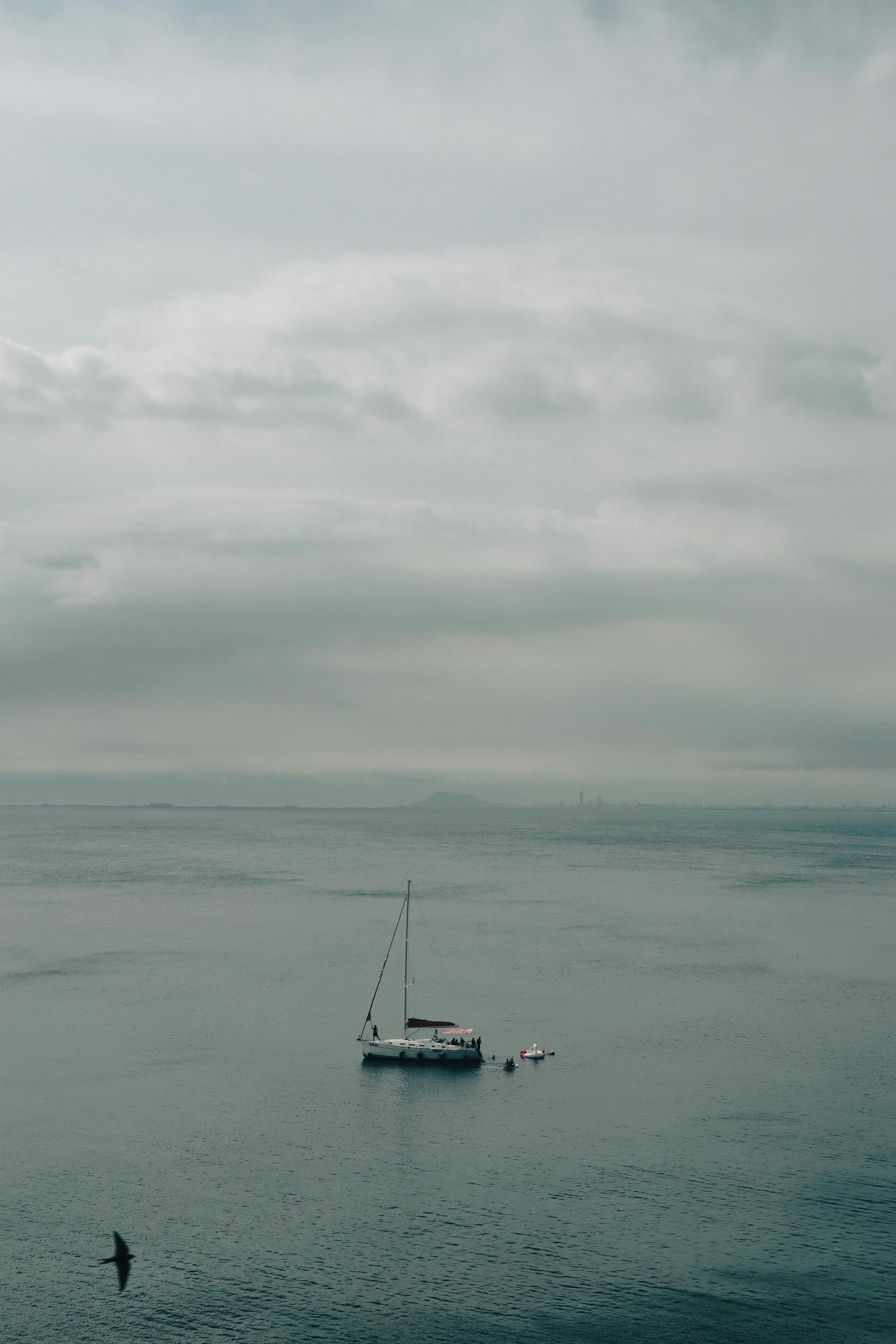 A lone sailboat drifts peacefully on the calm sea under a cloudy sky.