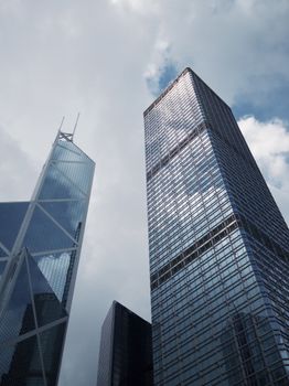 Low-angle view of modern skyscrapers with glass facades under a cloudy sky.