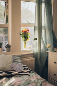 在阳光明媚的窗边，舒适的卧室角落里摆放着一瓶郁金香，窗帘柔软