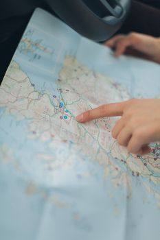 A woman's hand pointing at a location on a world map inside a car, highlighting navigation and travel planning.