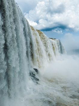 A breathtaking view of Iguazu Falls with powerful cascading waters and dramatic clouds.