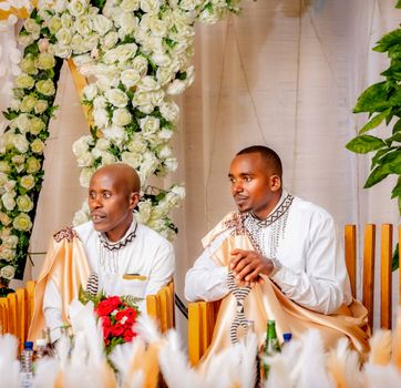 Men in traditional African attire at a cultural celebration surrounded by floral arrangements.
