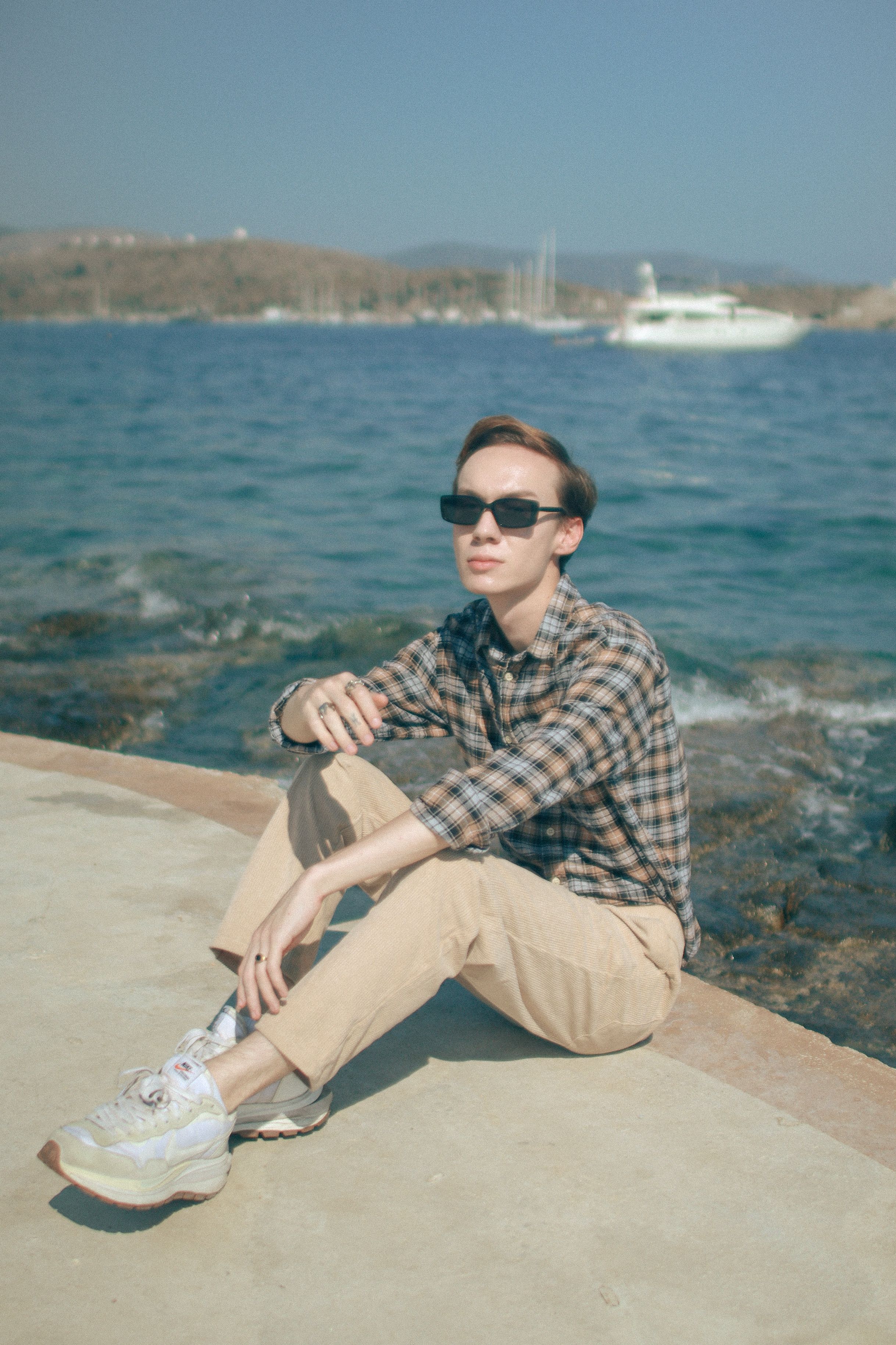 Young man in sunglasses sitting by the sea in Mugla, Turkey, enjoying a sunny day.
