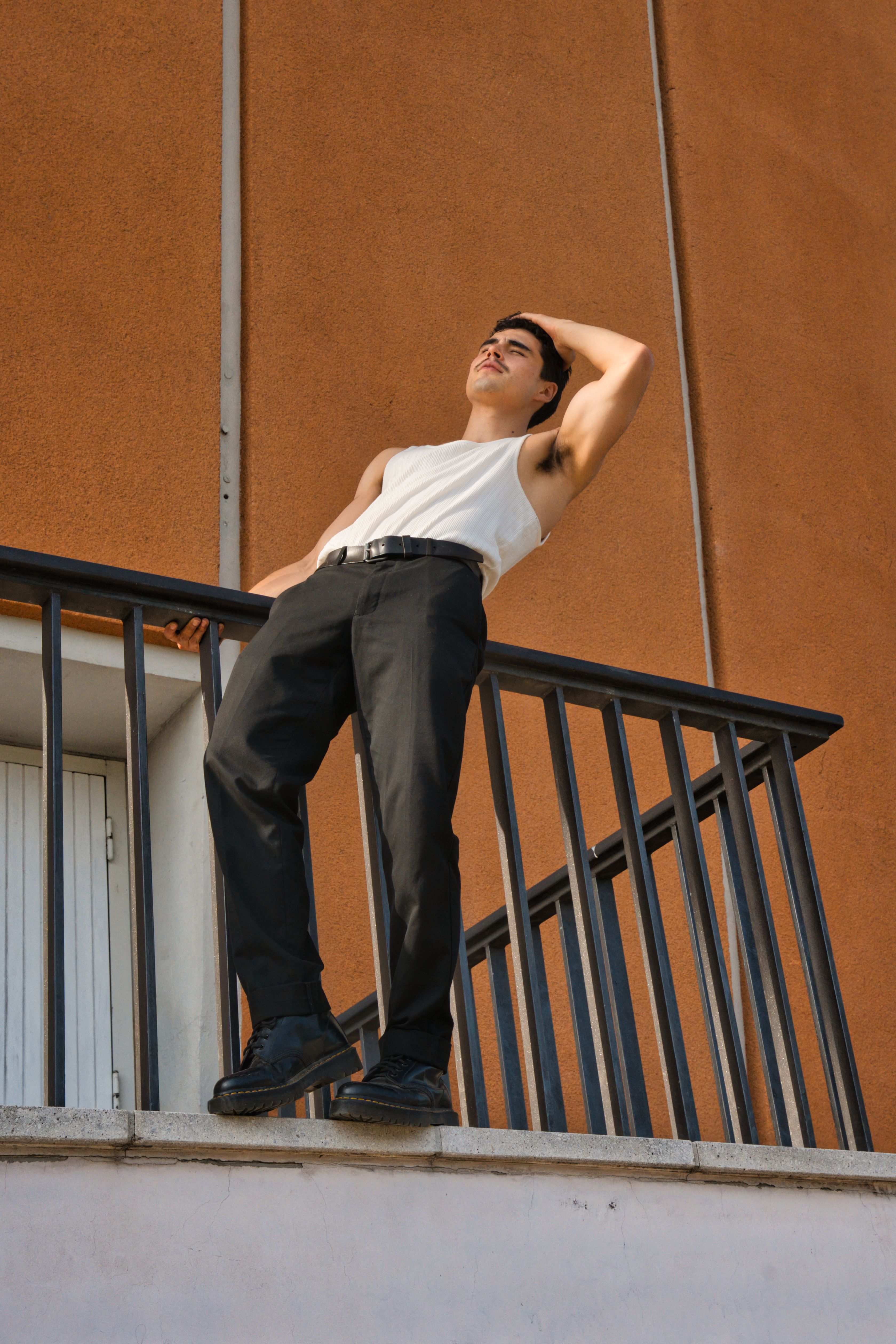 Fashionable man in a tank top and pants posing on a balcony in Berlin, Germany.