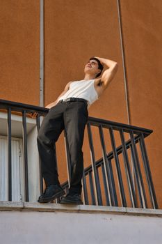 Fashionable man in a tank top and pants posing on a balcony in Berlin, Germany.