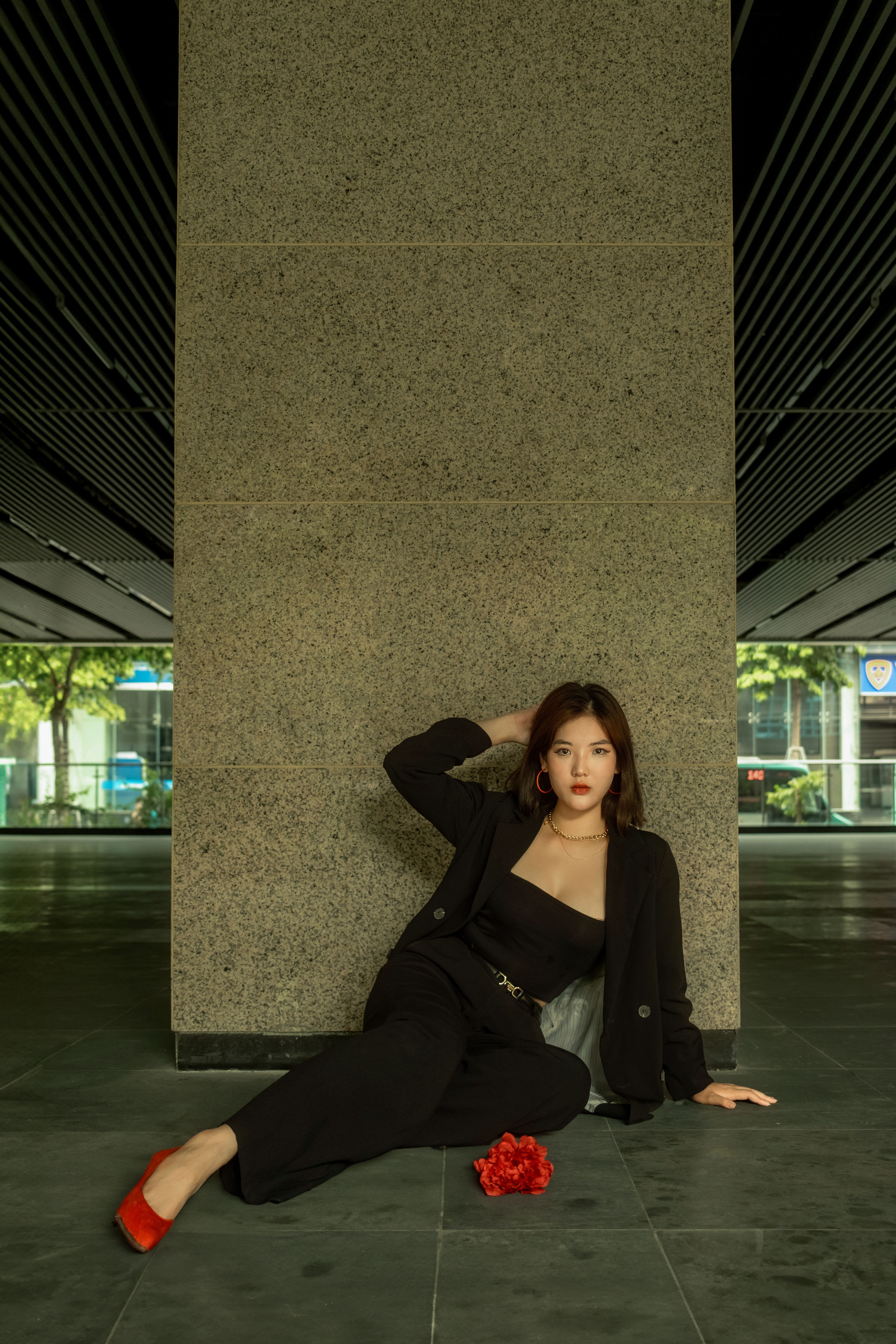 Elegant woman in black suit sitting against a wall, showcasing urban fashion.