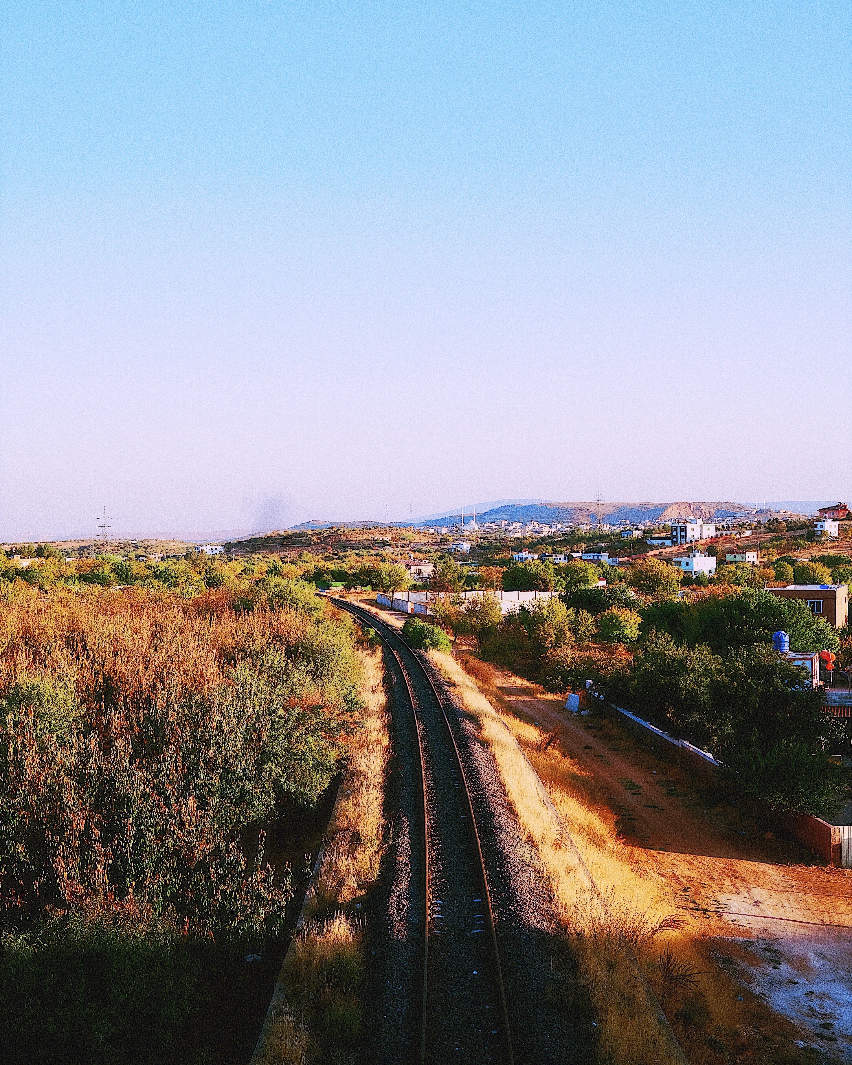 A railway track cutting through the lush rural landscape under a clear sky.
