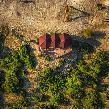 A bird's eye view of a rustic gazebo surrounded by greenery in a rural setting, captured with warm tones.