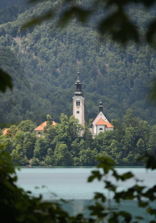 Free Scenic view of Bled's church surrounded by trees and lake waters, Slovenia. Stock Photo