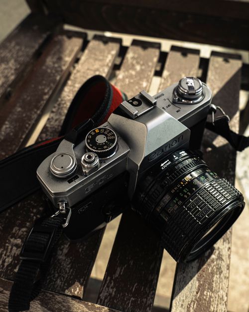 Free Classic film camera resting on an outdoor wooden bench, casting warm shadows. Stock Photo
