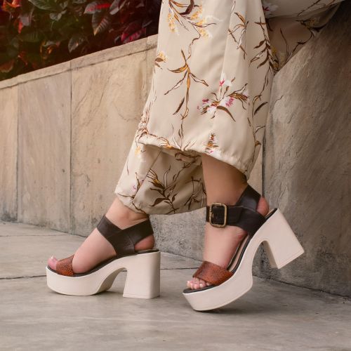 Free Elegant woman's feet in stylish platform heels and floral pants against a textured wall. Stock Photo
