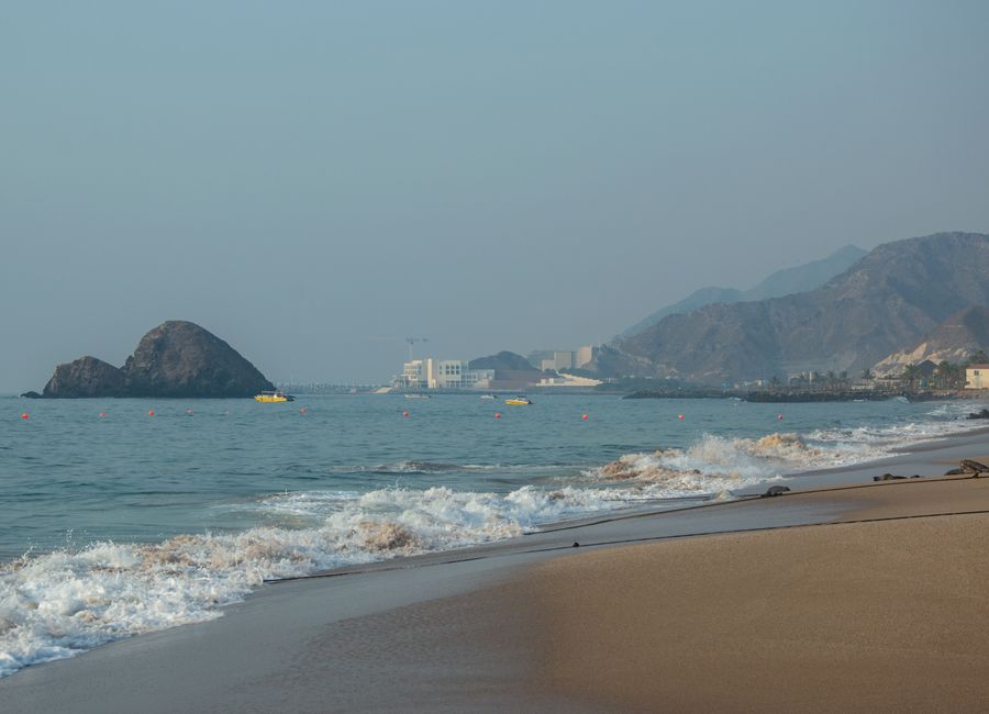 Peaceful beach scene with gentle waves, mountain backdrop, and clear horizon.