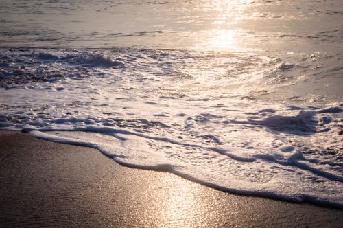 Free Golden sunlight reflecting on waves and sand at sunset, creating a serene coastal view. Stock Photo