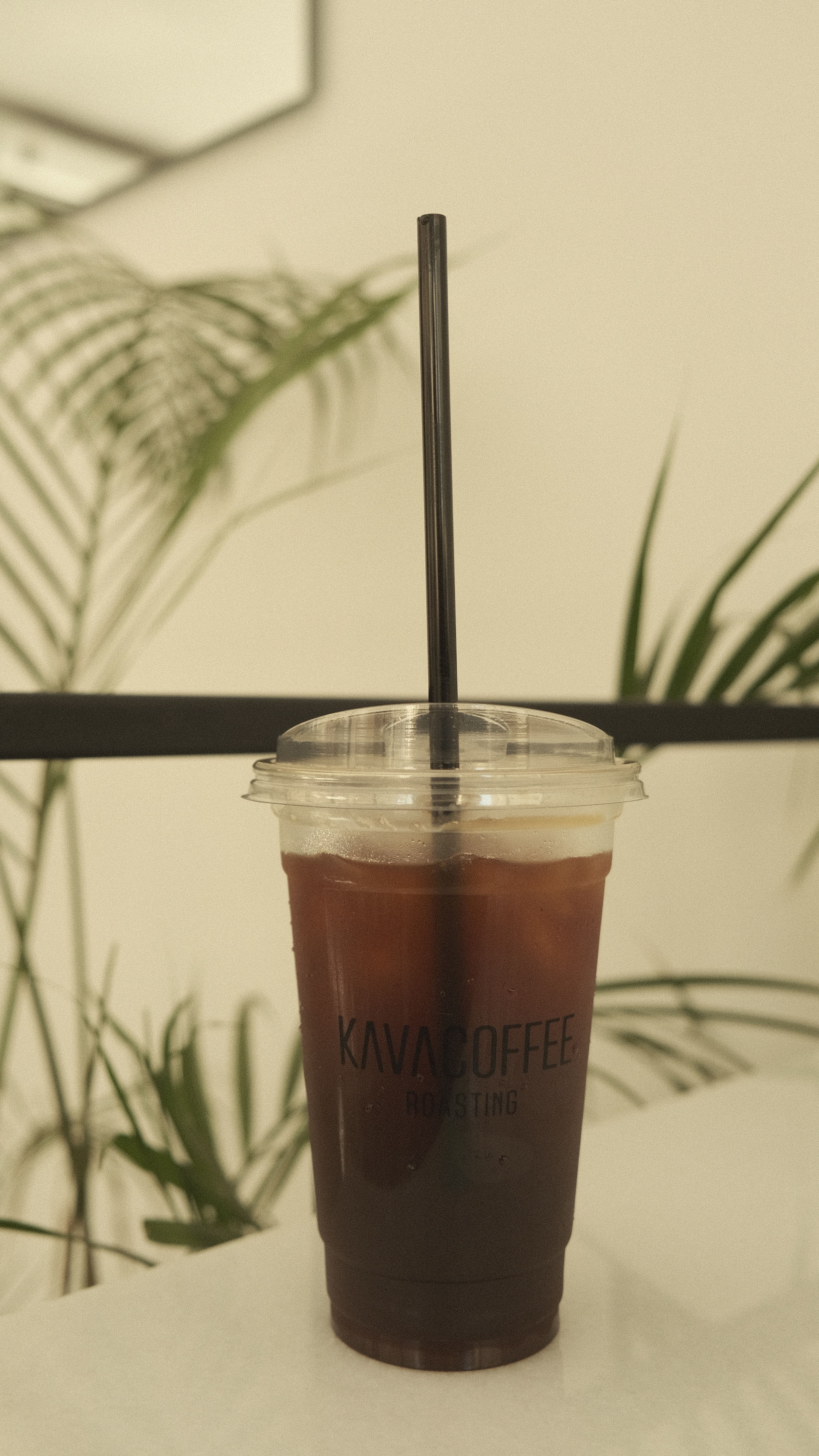 Refreshing iced coffee in a clear plastic cup with black straw, indoor cafe setting.
