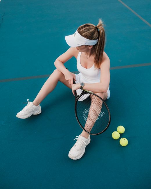 Woman in sports attire sitting on tennis court with racket and balls.