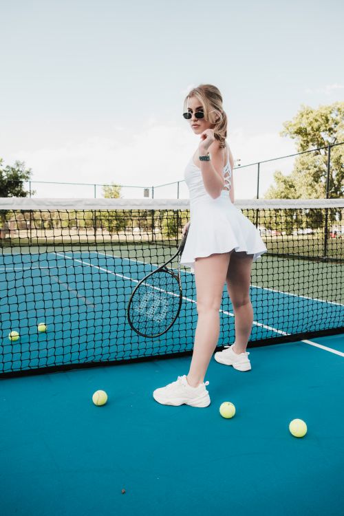 Free Confident woman in sportswear poses on a blue tennis court holding a racket with tennis balls around. Stock Photo