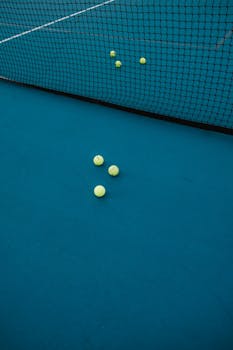 Tennis balls scattered on a blue tennis court with visible netting, capturing sports essence.