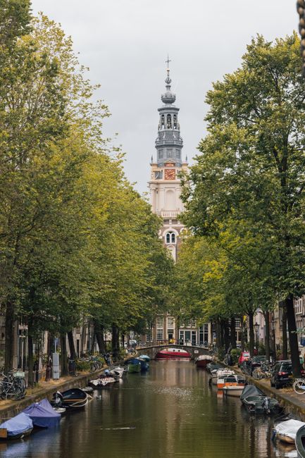 Charming view of Amsterdam canal leading to the iconic Westerkerk tower, surrounded by lush greenery.