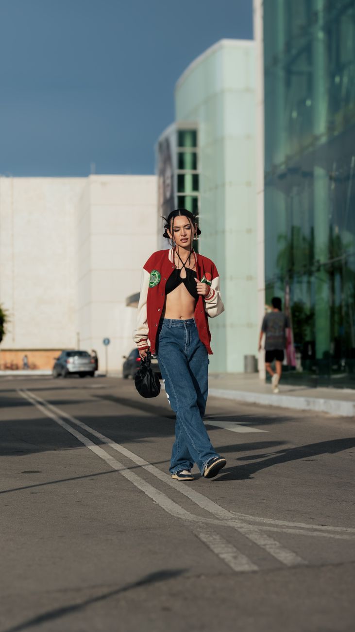 Trendy woman in jeans and a jacket walking confidently in a city setting. Urban fashion highlighted.