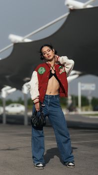 Young woman in trendy streetwear posing confidently outdoors with denim and jacket.