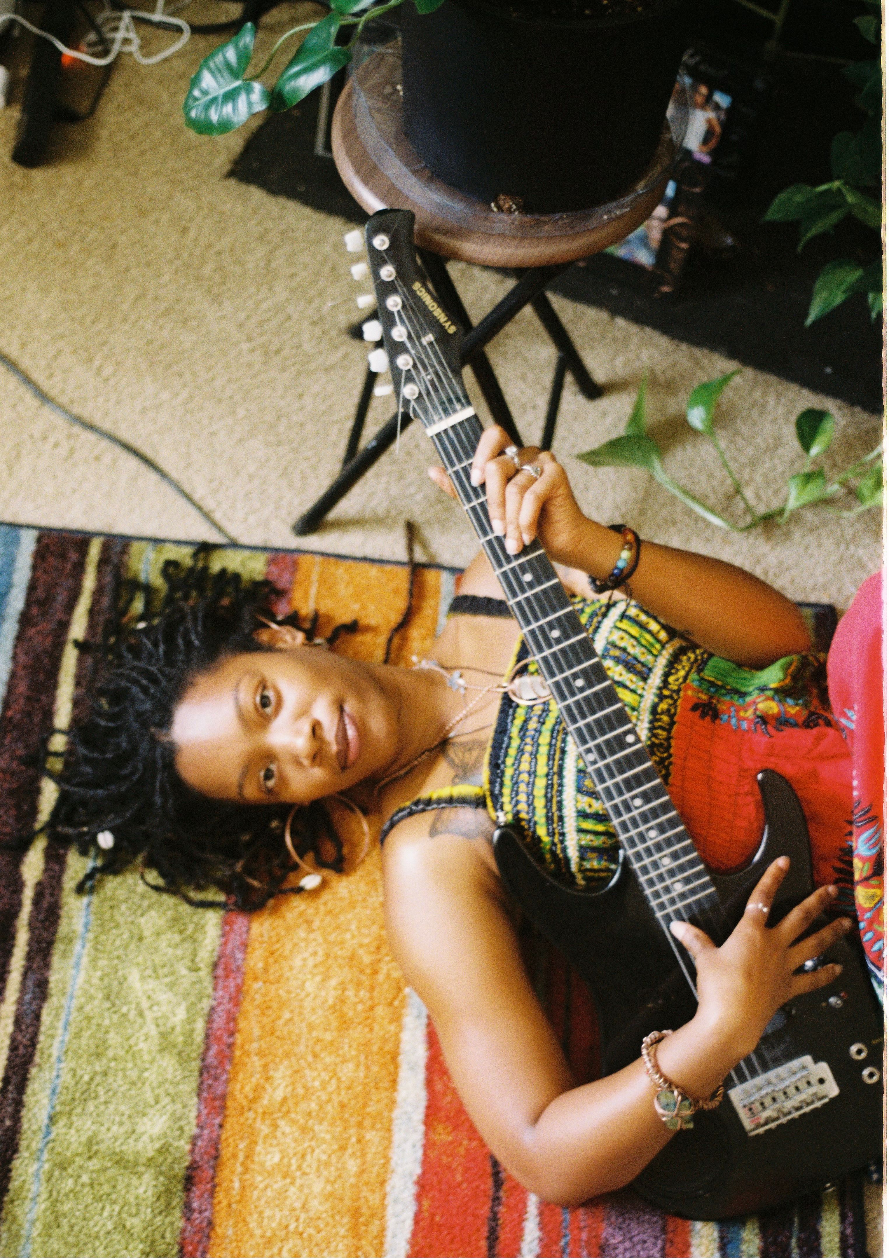 Young woman lying on a colorful rug, holding an electric guitar indoors in Atlanta, GA.