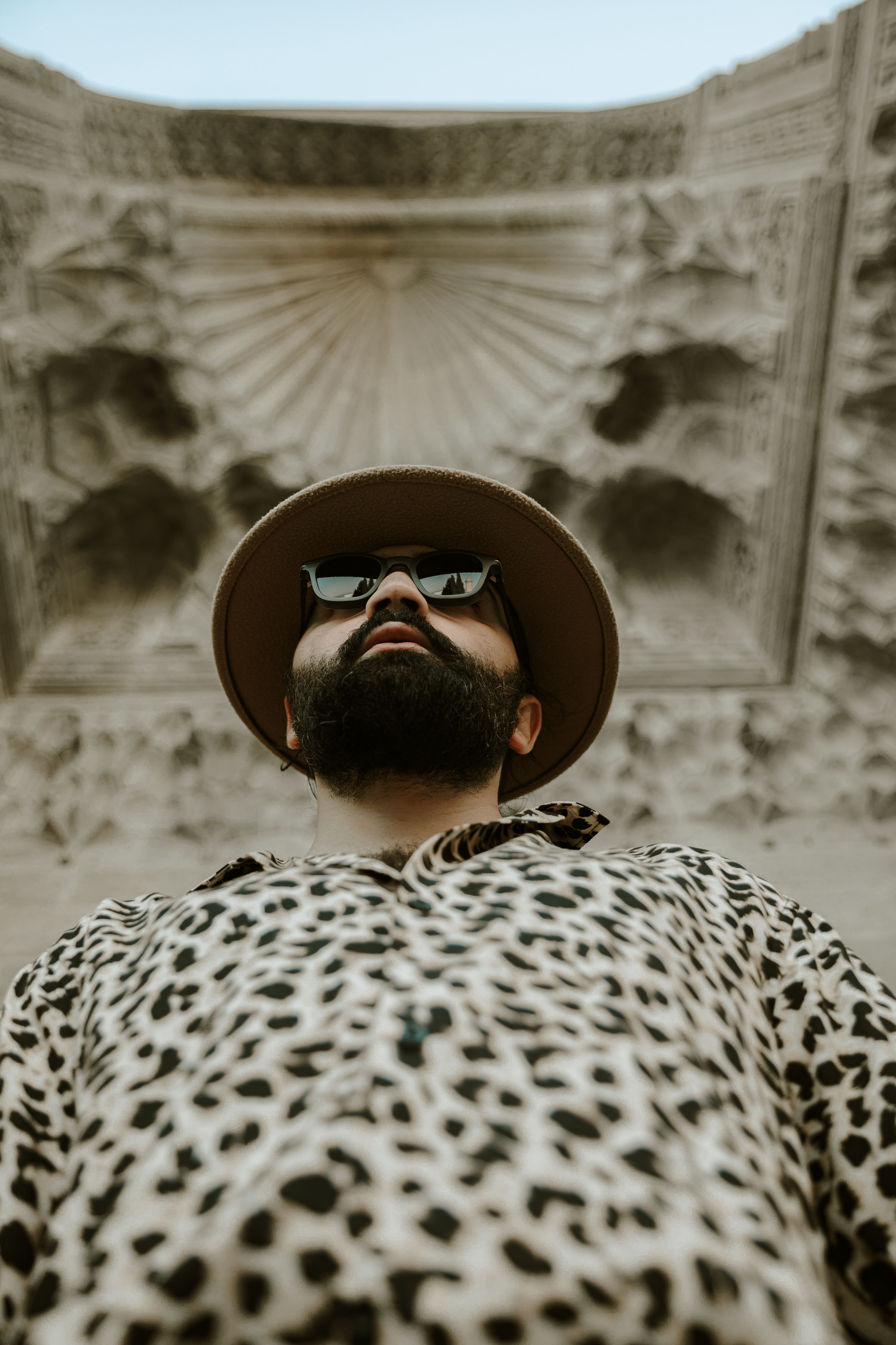Fashionable man with sunglasses and hat posing in front of intricate architecture in Baku.