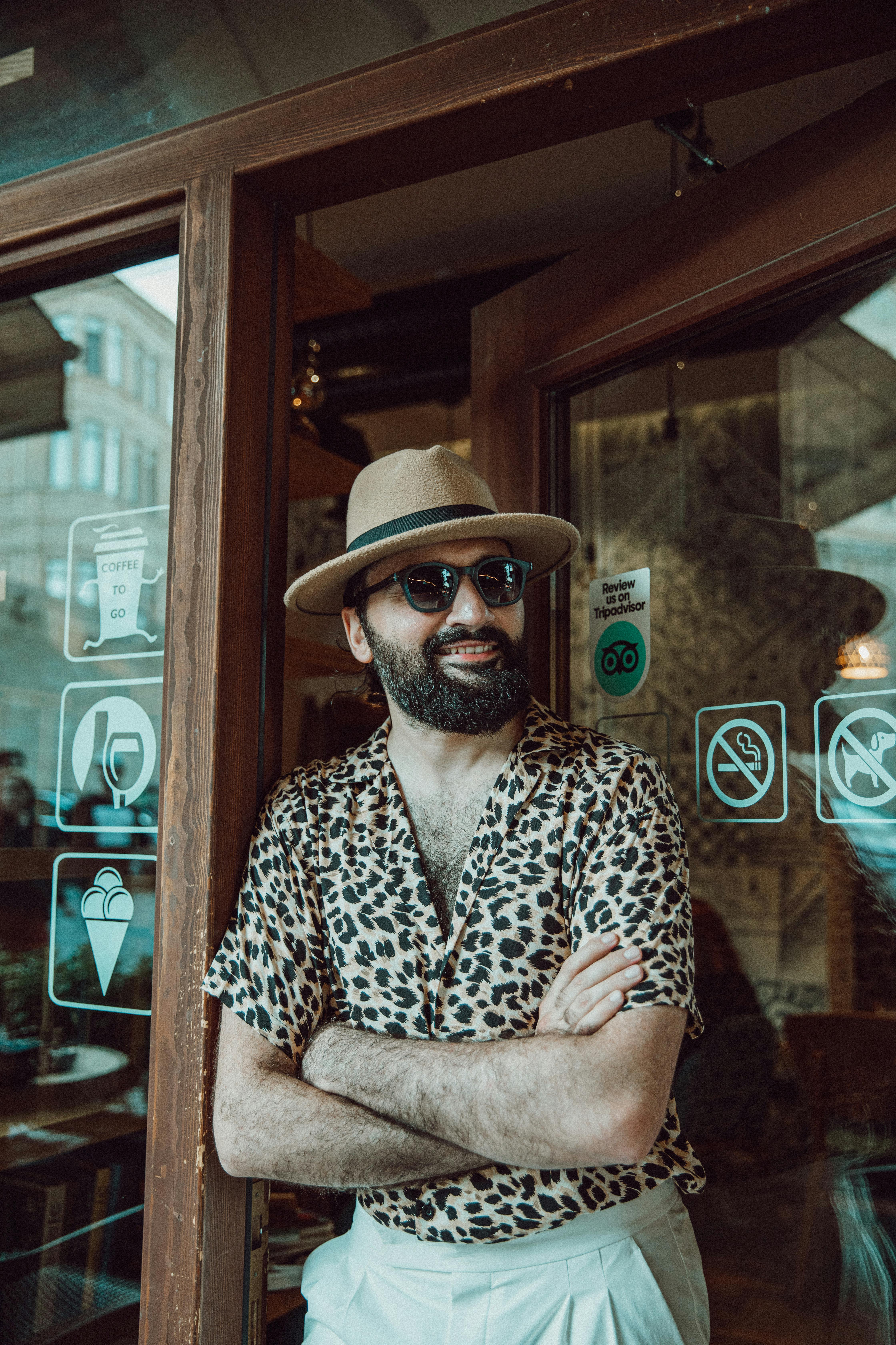 Stylish man with sunglasses and hat smiling by cafe entrance in Baku, Azerbaijan.