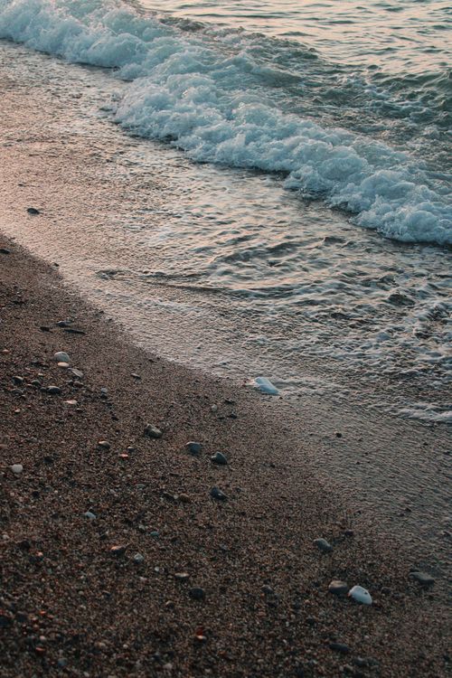 Free Peaceful waves and sandy beach create a calm coastal scene during sunset. Stock Photo