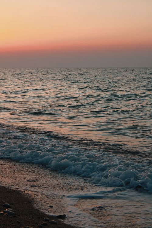Free Peaceful sunset on an ocean shore with gentle waves and a vivid horizon. Stock Photo