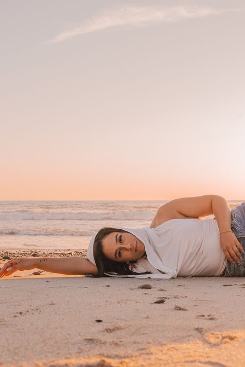 Free A woman in a white blouse and jeans lying on Esposende Beach as the sun sets. Stock Photo
