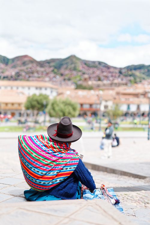 Free A person in traditional Quechua attire sits in Cusco's main square, Peru, under a vibrant sky. Stock Photo