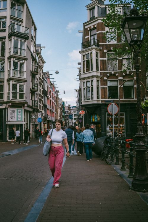 Free A woman walking along a picturesque street in Amsterdam, showcasing classic Dutch architecture. Stock Photo