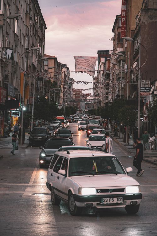 Free Cars and pedestrians fill a busy city street under a colorful sunset sky. Stock Photo