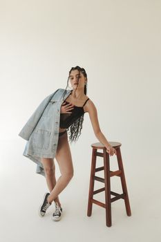 Fashion portrait of a woman wearing a denim jacket, posing with a stool in a studio setting.