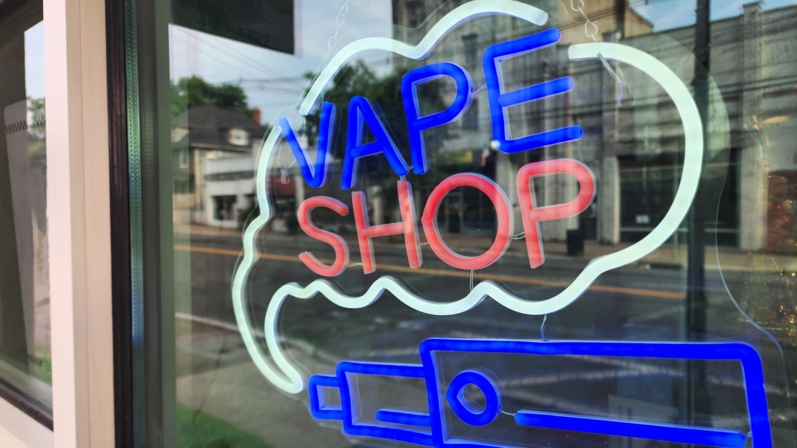 Bright neon sign of a vape shop in a city window reflecting the urban street.