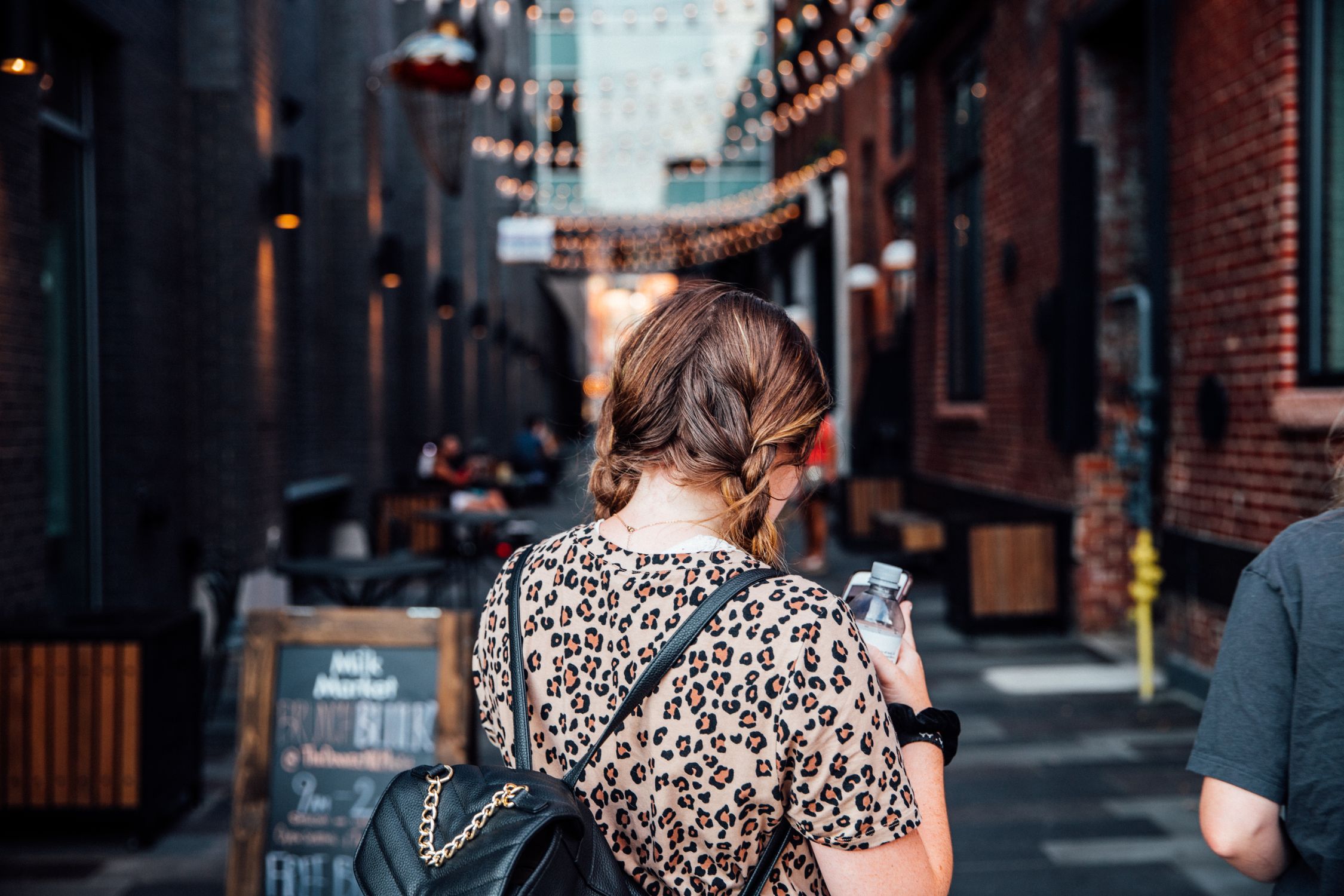 Back view of a woman with braided hair strolling through a lively alley in Denver, CO.