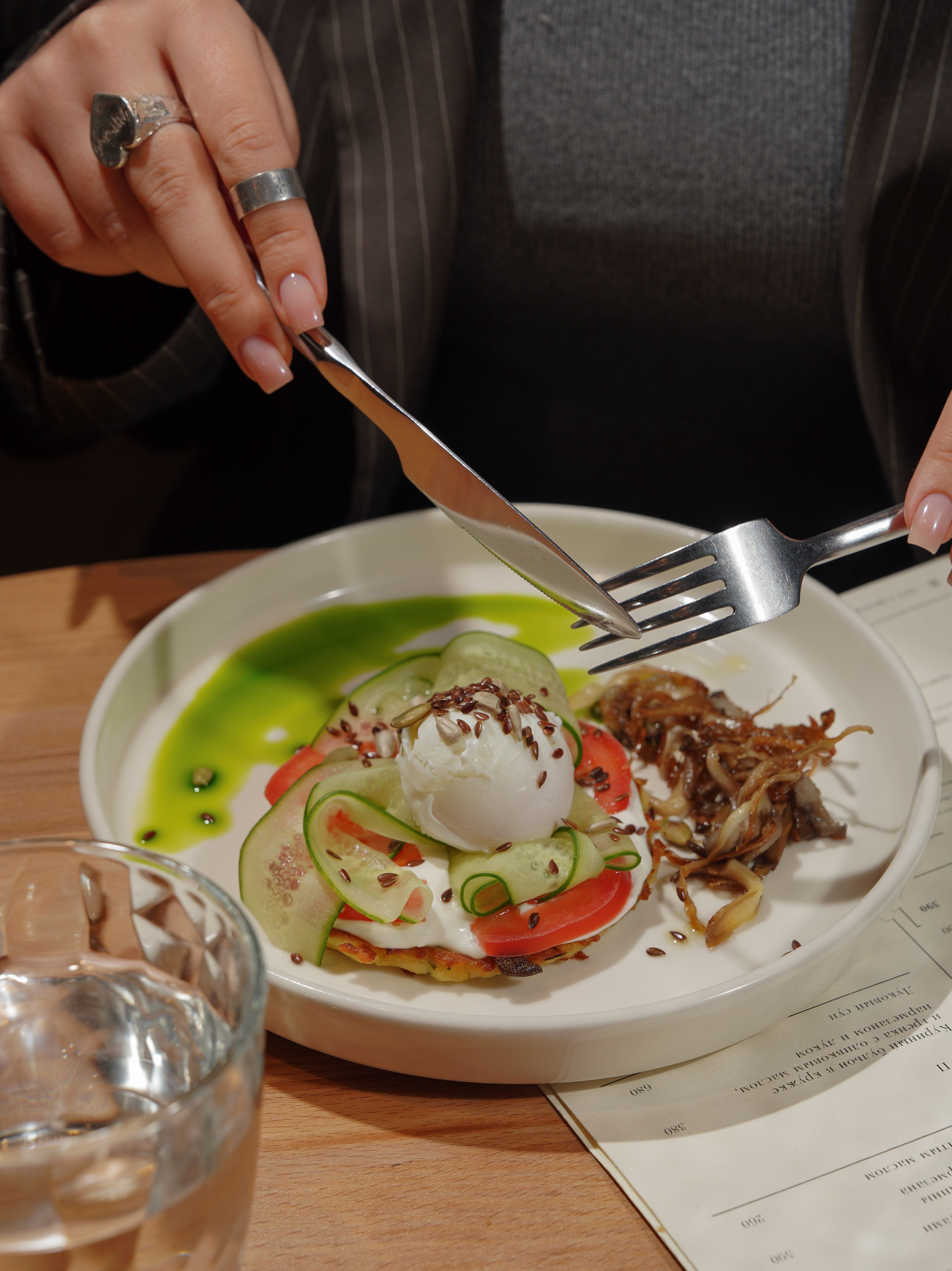 Delicious gourmet dish featuring poached egg, cucumber, and tomato with a side of greens, perfect for breakfast.