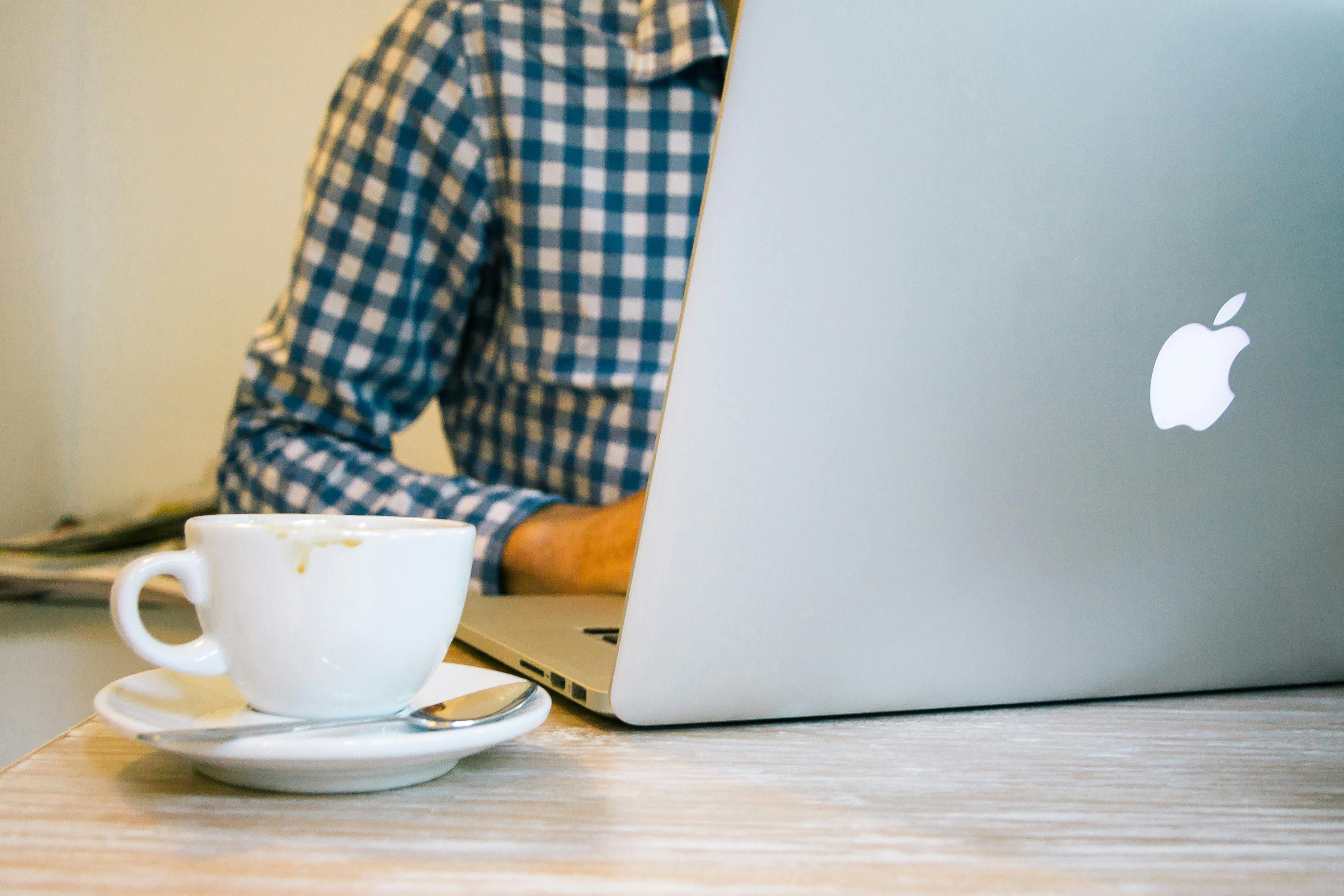 White Ceramic Teacup Beside Silver Macbook on Table