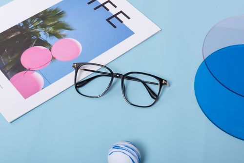 Free Black eyeglasses on a blue background with a vibrant magazine and abstract shapes. Stock Photo