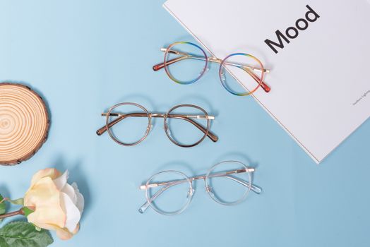 Flat lay of stylish eyeglasses and Mood magazine on a light blue backdrop.