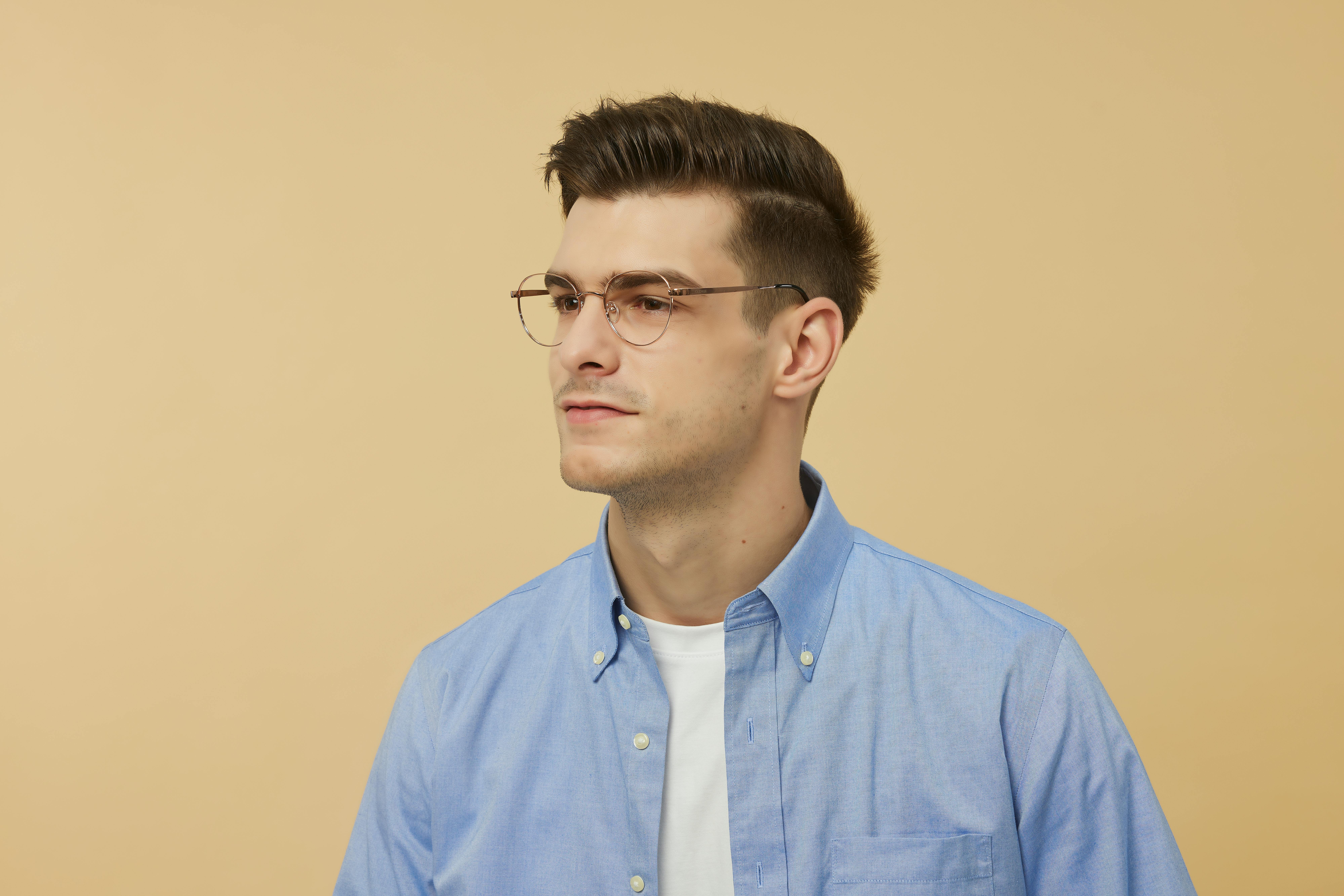 Free Portrait of a young man wearing eyeglasses and a blue shirt, looking serious against a neutral background. Stock Photo